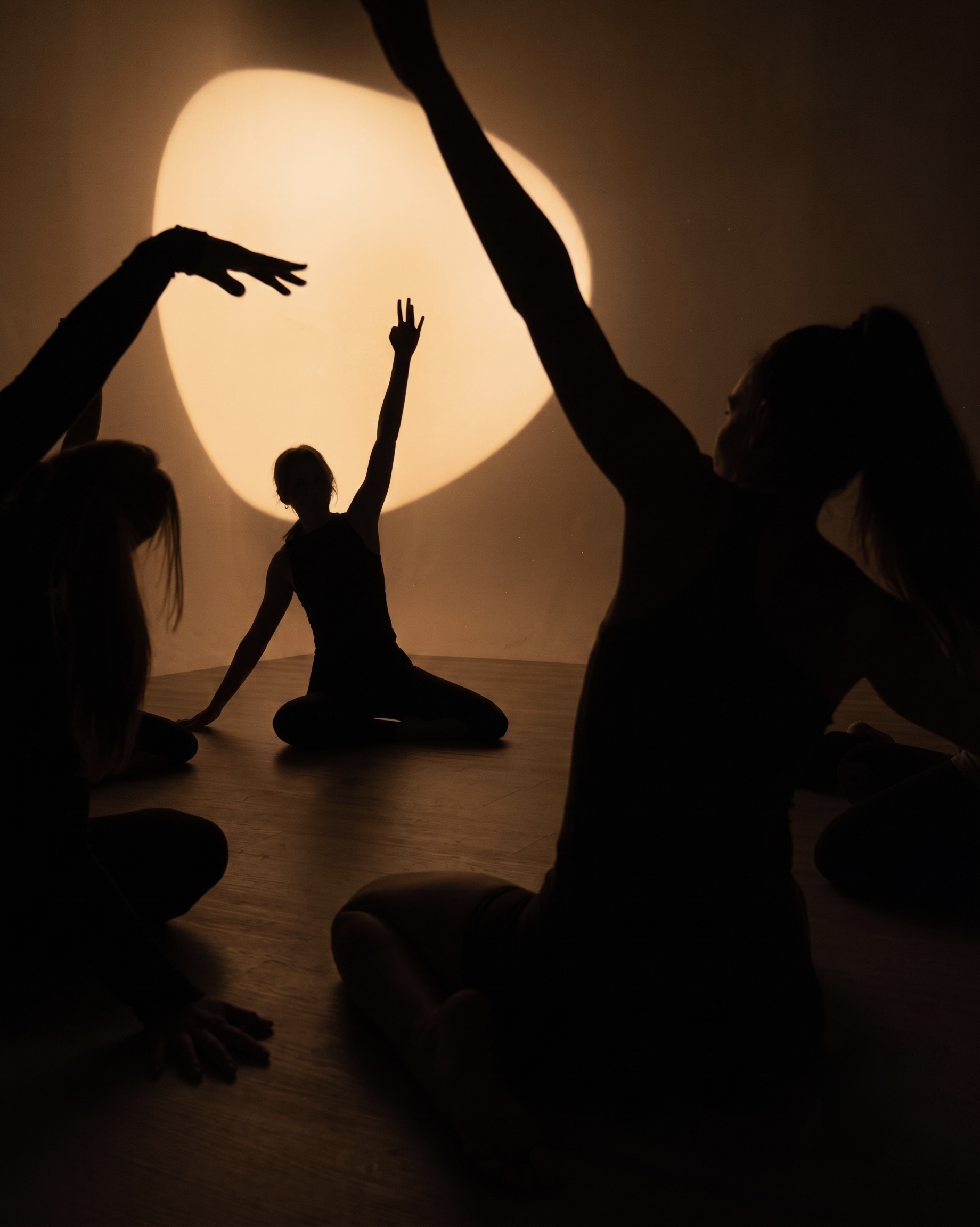 Silhouettes of women stretching in a dark room lit by a round warm light